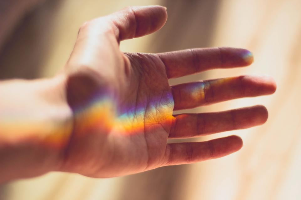 Mano abierta que recibe un haz de luz con los colores del arcoíris