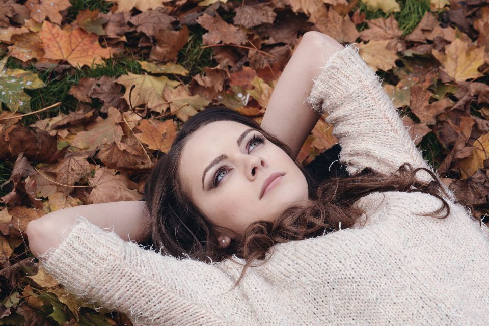 Mujer tumbada sobre hojas de otoño, pensativa