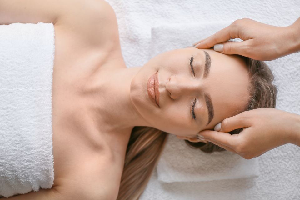 Manos de una terapeuta apoyadas con suavidad sobre la cabeza de una mujer que descansa con los ojos cerrados