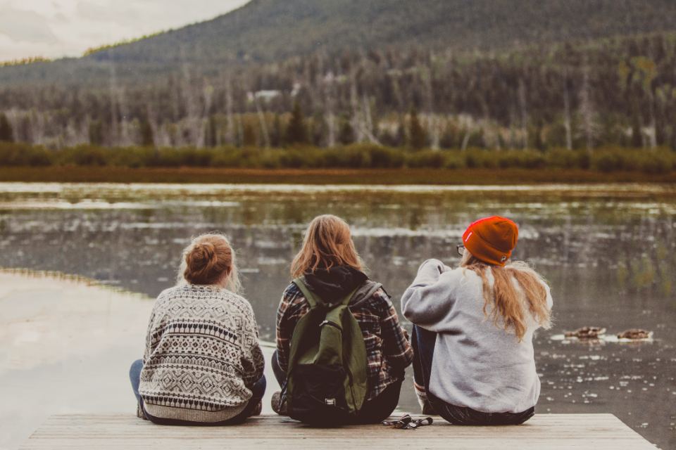Tres personas sentadas juntas a la orilla de un lago, de espaldas